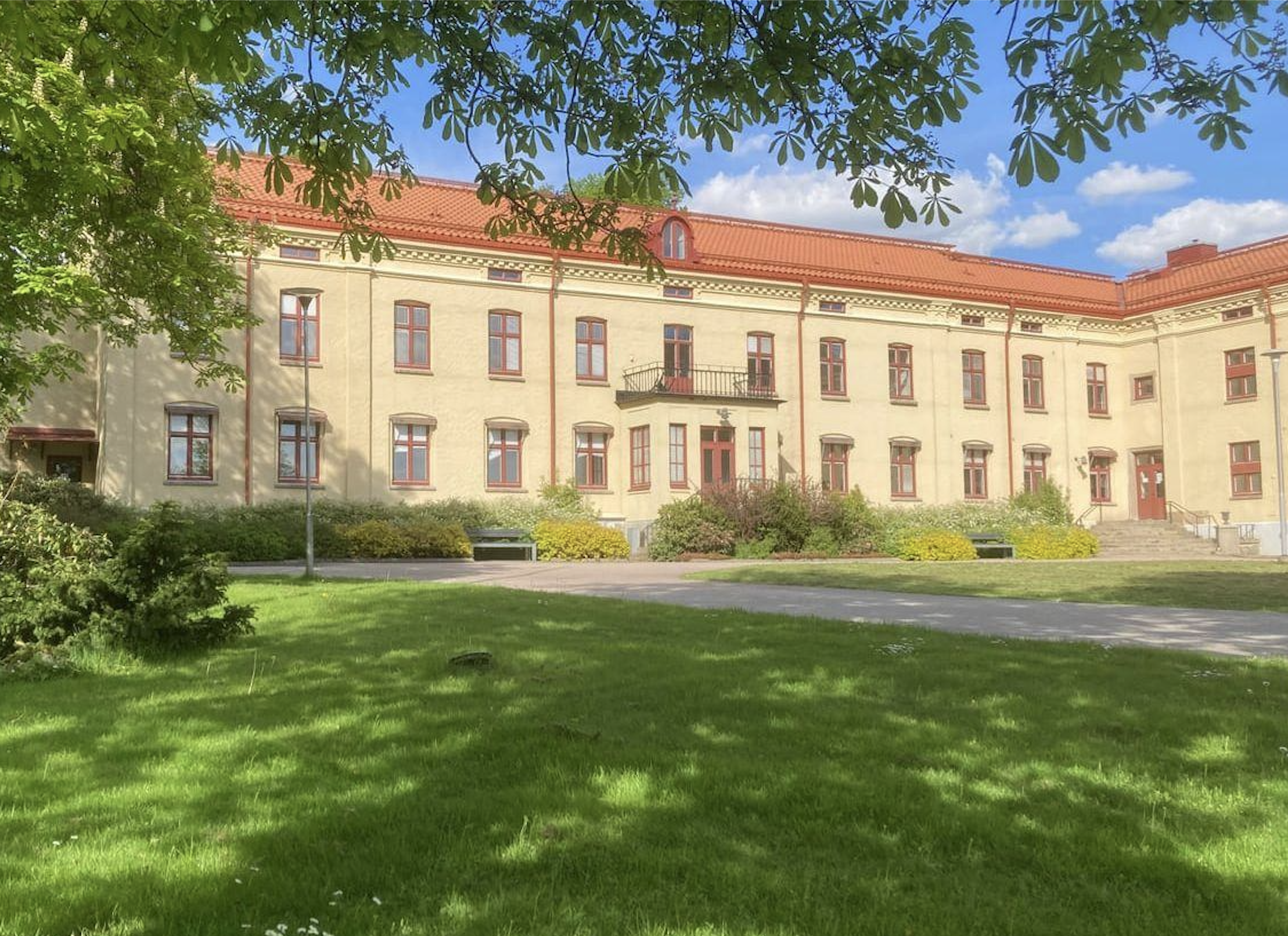 Stavregårdens gula huvudbyggnad med rött tegeltak, sedd från parken en sommardag