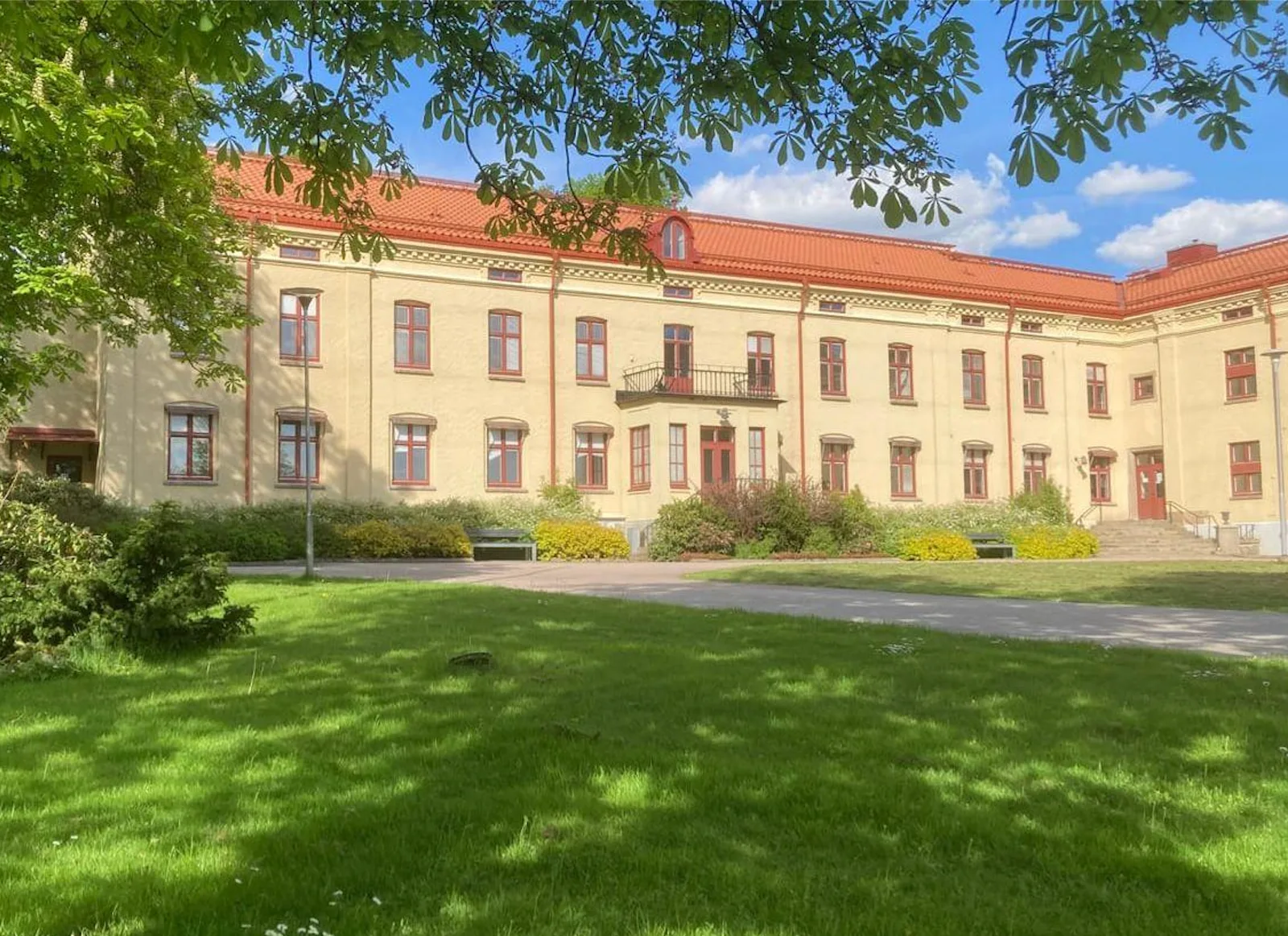 Stavregårdens gula huvudbyggnad med rött tegeltak, sedd från parken en sommardag